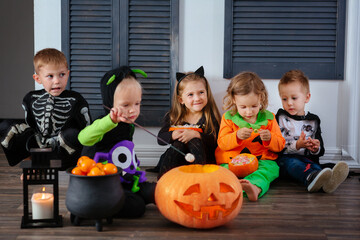 four kids in carnival costumes are celebrating Halloween, and playing with pumpkins and candies and roasts marshmallow