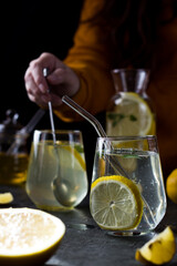 A woman makes lemonade. Pieces of lemons, a jug and glasses stand on the table on a black background