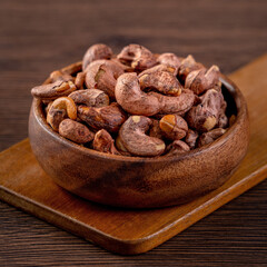 Cashew nuts with peel in a wooden bowl on wooden tray and table background, healthy raw food plate.