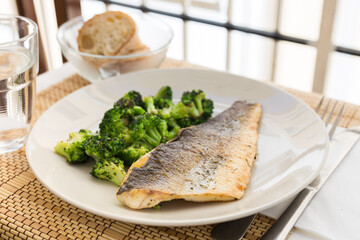 fried fillet of sea bass with garnish of broccoli on black warm stone plate