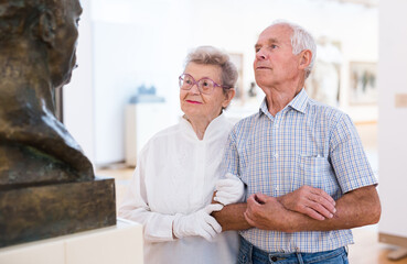 mature European couple examines paintings in an exhibition in hall of art museum