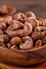 Cashew nuts with peel in a wooden bowl on wooden tray and table background, healthy raw food plate.