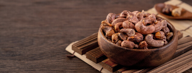 Cashew nuts with peel in a wooden bowl on wooden tray and table background, healthy raw food plate. - Powered by Adobe