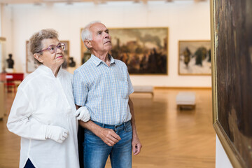 Fototapeta premium mature European couple examines paintings in an exhibition in hall of art museum