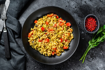 Bulgur with vegetables, onions, sweet peppers, carrots and parsley in a plate. Black background. Top view