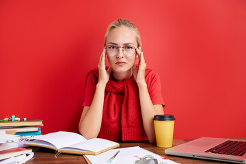 young caucasian disillusioned woman needs some rest at work, she has a lot of work deadlines, sits at table with laptop, think. isolated red background