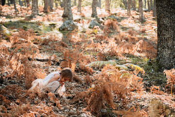 Little caucasian baby girl squatting in the forest among ferns
