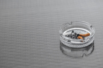Close-up of an ashtray with cigarette butts. Glass cigarette ashtray on the table. Three filter...