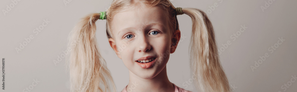 Wall mural Closeup portrait of surprised sad Caucasian girl on light background. Child with long pig tails hair posing looking in camera. Kid expressing positive emotion. Web banner header.