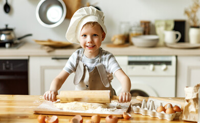Happy kid preparing dough at home.