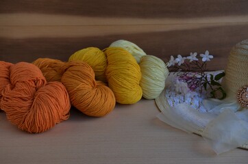 Madejas de hilo de colores para tejer, sobre fondo textura madera con flor blanca y sombrero.