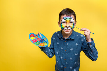 Cute boy with faceart on birthday party, colorful tiger holding palette with gouache isolated on...