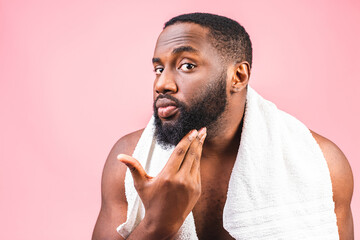 African American man smears shaving cream on face by shaving brush. Male hygiene. Isolated on pink...