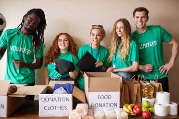 young enthusiastic volunteers with donations for poor people, cardboard box with clothes for...