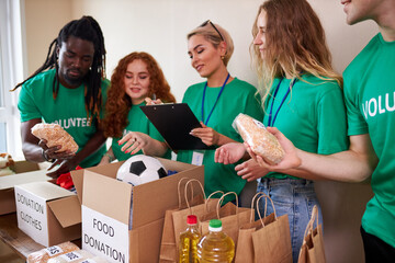 happy young volunteers donating clothes and food for charity, indoors. active ethusiastic volunteering team putting stuff into boxes for poor people. kindness and generosity concept