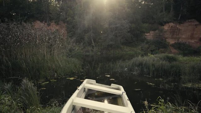 A white plastic boat sank near the banks of the Salaca River. Against the background of red sandy rocks. Reeds and trees are illuminated by the autumn sun. Latvia