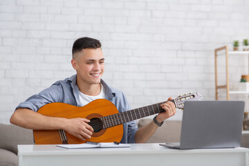 Online music lesson at home and leisure time during COVID-19 outbreak. Happy guy with guitar looks...