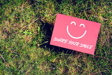 Share your smile message written on paper on grass background. Inspirational quote for motivation, happiness or positive vibes in relationships or life.