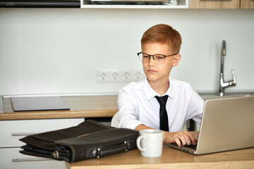 young caucasian business boy work from home using laptop, he is in formal wear, suit, in eyeglasses. intelligent boy is pretend to be adult