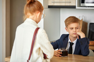 young little caucasian kids couple at home, boy is drinking tea, tired of work, get some relax at home. in the kitchen, with redhead girl came from work