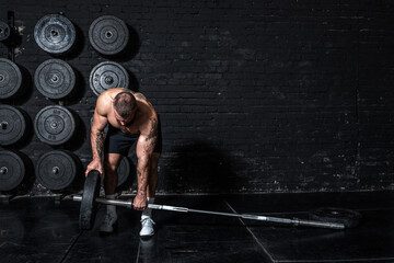 Young sweaty strong muscular fit man with big muscles putting heavy iron weight plate on the...