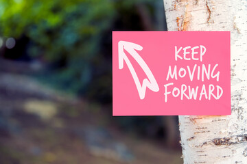Keep moving forward inspirational quote written on paper on a tree in nature. Persistence, progress...