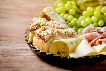Appetizers antipasti with white sicilian focaccia. Traditional bread sliced cake with onion served with prosciutto ham, cheese, grapes over wooden background. Close up