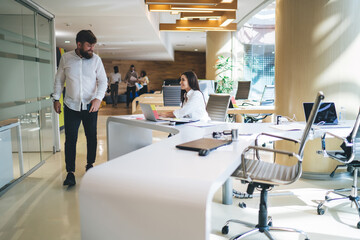 Caucasian woman doing distance job in coworking space for freelancers communicate with friendly smart casual man, skilled woman enjoying digital marketing at netbook and live talking with partner