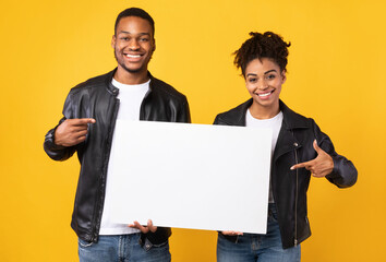 African Couple Showing Poster Pointing Fingers At Copyspace, Yellow Background