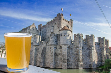 Glass of light beer on wooden table with view of Castle of the Counts in Ghent, Belgium