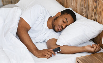 Fototapeta premium African American Man Sleeping Holding Smartphone Resting In Bed Indoor