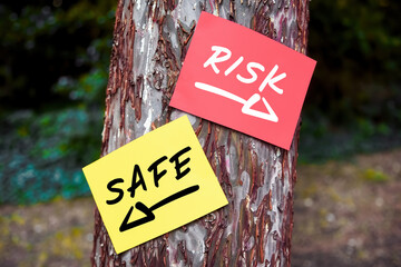 Risk versus safe words written on papers on a tree with arrow signs. Taking the risky way or secure...