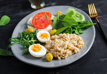 Breakfast oatmeal porridge with boiled egg, tomatoes sandwich, arugula and spinach. Healthy food.