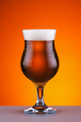 foamy cold amber beer in a beautiful glass in hot weather