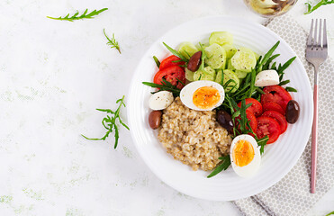 Breakfast oatmeal porridge with greek salad of tomatoes, cucumbers, olives and eggs. Healthy balanced food. Top view, flat lay, copy space