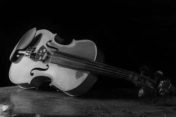 Old and beautiful violin on a rustic wooden surface and black background low key portrait,...