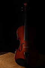 Old and beautiful violin on a rustic wooden surface and black background low key portrait,...