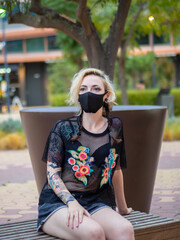 Woman wearing a medical mask sitting on a bench - new normal