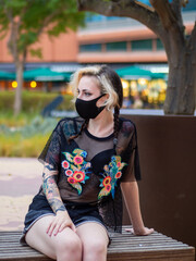 Woman wearing a medical mask sitting on a bench - new normal