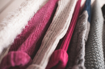 Knitted colorful clothes hang on rack indoors in shop. Season sale time. Selective focus.