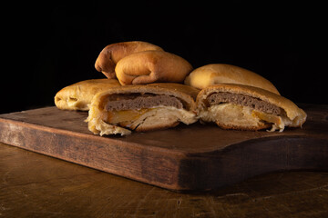 Homemade bread stuffed with hamburger, cheese and tomato, on a cutting board with black background....