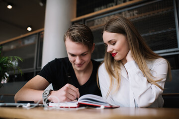 Cheerful man with woman writing in notebook in cafe