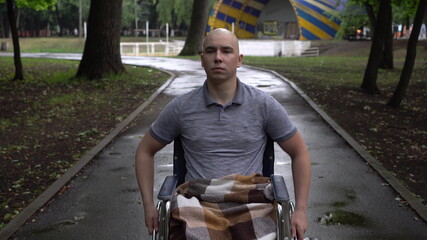 A young man with oncology rides a wheelchair through the park. The man is bald due to chemotherapy.