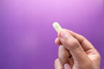 hand holding pills on purple background with copy space 