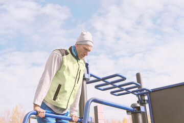 middle aged man doing push ups on parallel bars in openair gym. autumn active lifestyle. outdoors sport in a cold season. sports and leisure during fall and winter. caucasian man on a sports ground.