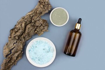 Sea salt, serum in brown dropper glass, clay mask and tree bark flat lay on blue background top view. Spa products composition. Organic, bio, natural body cosmetic. Beauty, skincare concept.