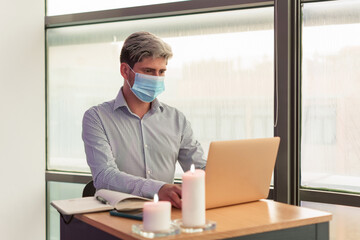 Man working with his laptop in his office, wearing a sanitary mask due to the covid virus.
