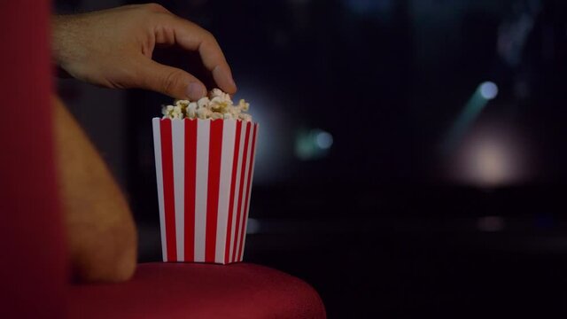 Eating popcorn while watching a movie on the couch at home.