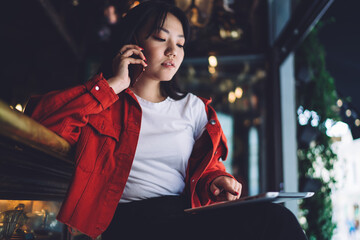 Thoughtful young woman talking on smartphone and using tablet