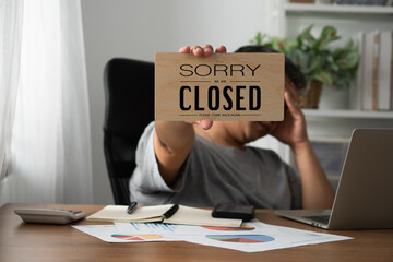 The owner of the business is stressed and disappointed. And holding a sign to close the business after the revenue and cost was raised and recognized the loss